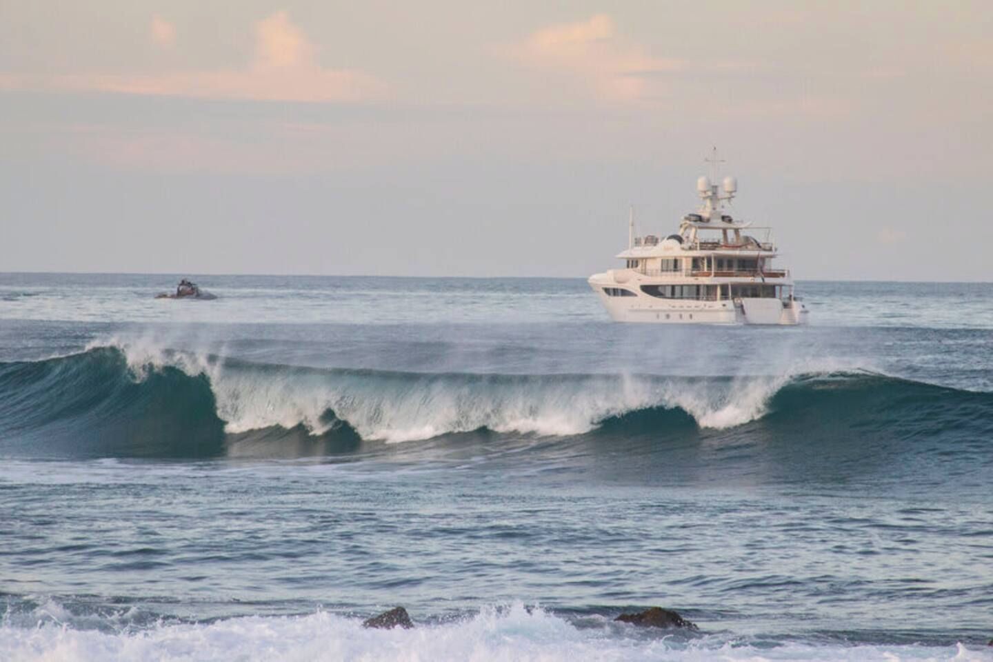 A large yacht with multiple decks and a helipad, sailing on a sea with waves.