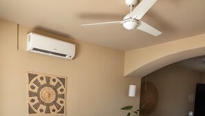 A living room with a sofa, a coffee table, a ceiling fan, and a wall-mounted air conditioner. - Elegant Oceanview Suite Perfect Hideaway for two (La Majahua)