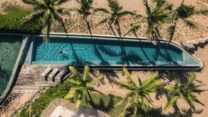 An aerial view of a rectangular swimming pool surrounded by palm trees and a wooden deck with lounge chairs. - Elegant Oceanview Suite Perfect Hideaway for two (La Majahua)