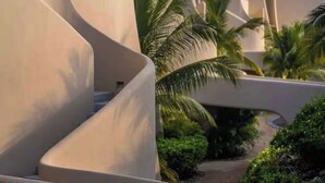 A modern resort with curved architecture, palm trees, and a clear sky. - Elegant Oceanview Suite Perfect Hideaway for two (La Majahua)