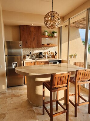 Una cocina con una isla central, armarios de madera, un refrigerador de acero inoxidable y una lámpara colgante.