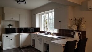 Una cucina con mobili bianchi, un forno a microonde, una macchina da caffè, un lavello e una finestra vista alberi.