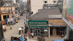 Une rue animée bordée de commerces, notamment une pharmacie et une boutique de verrerie.