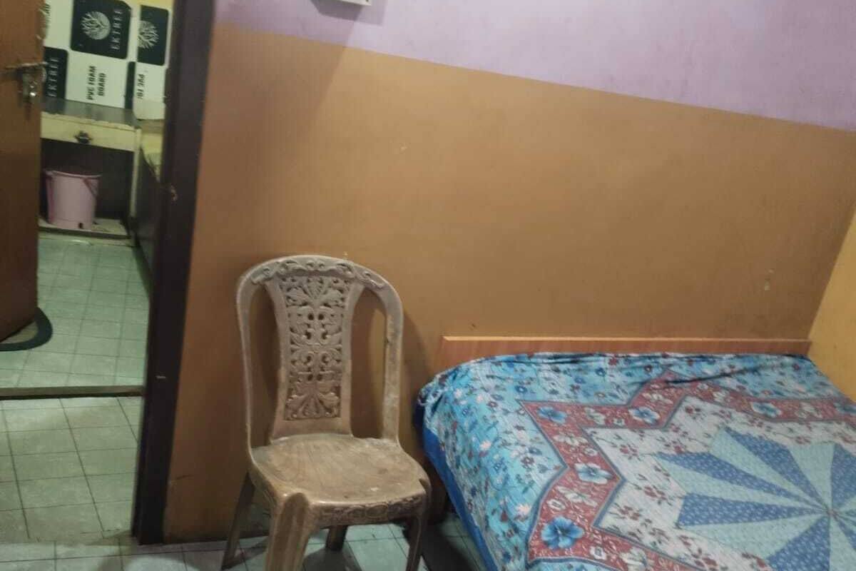 A room with a bed, a chair, a wall socket, and a door leading to another room.