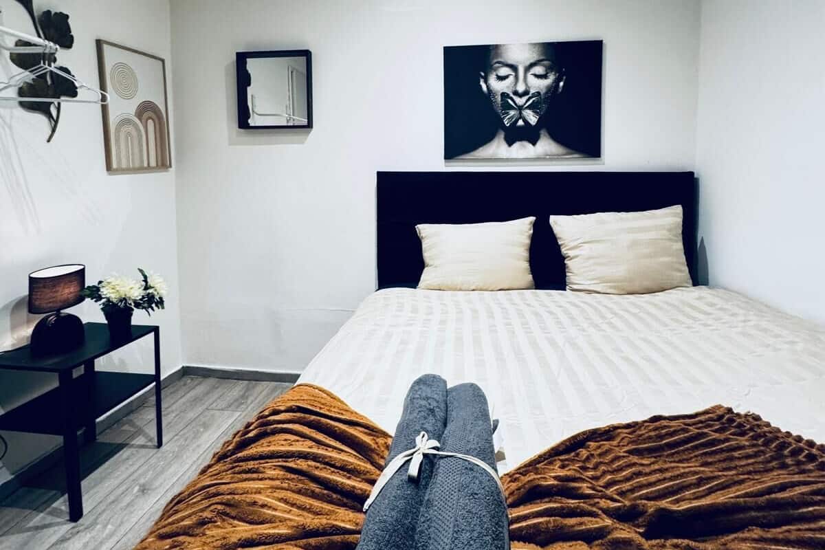Quarto com cama, mesa de cabeceira, luminária e obra de arte na parede.