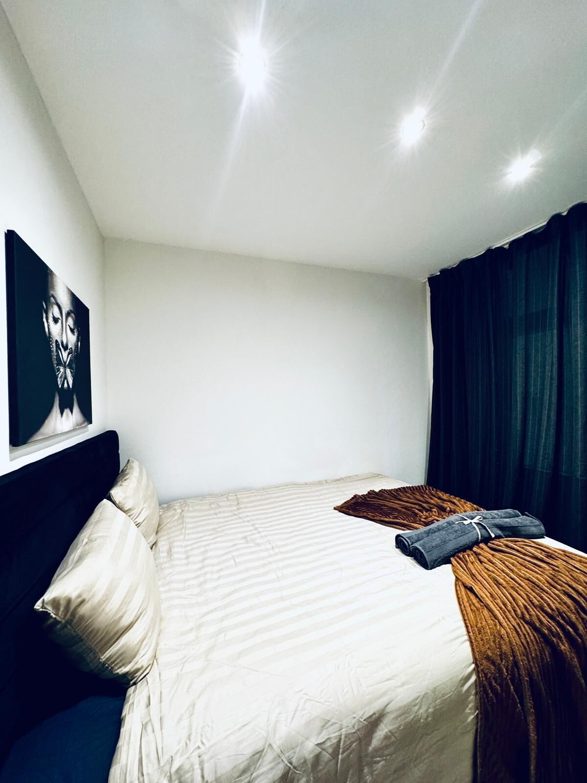 Una habitación de hotel con una cama, cabecero, una obra de arte en la pared y una ventana con cortinas.