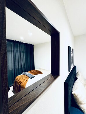 Ein Schlafzimmer mit einem großen Spiegel, einem Bett mit Kopfteil, einem Fenster mit Vorhängen und einem Wandbild.
