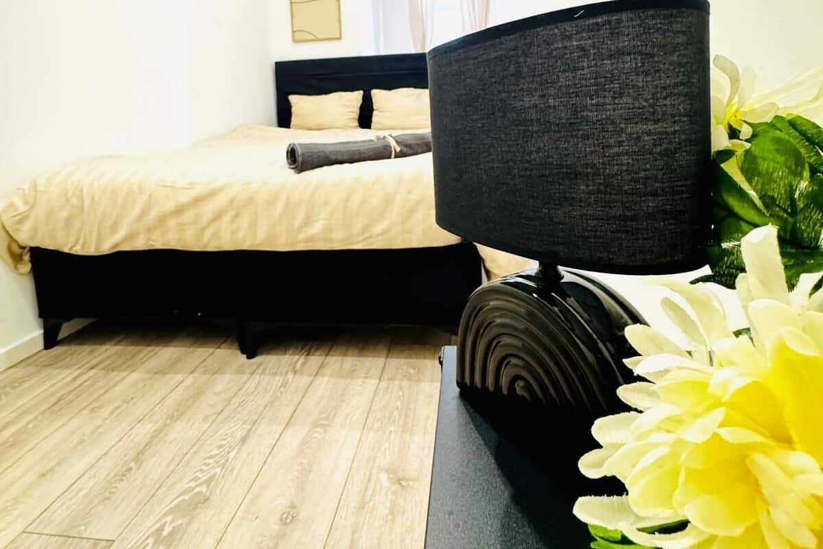 Um quarto moderno com uma cama, uma mesa de cabeceira com abajur e piso de madeira.