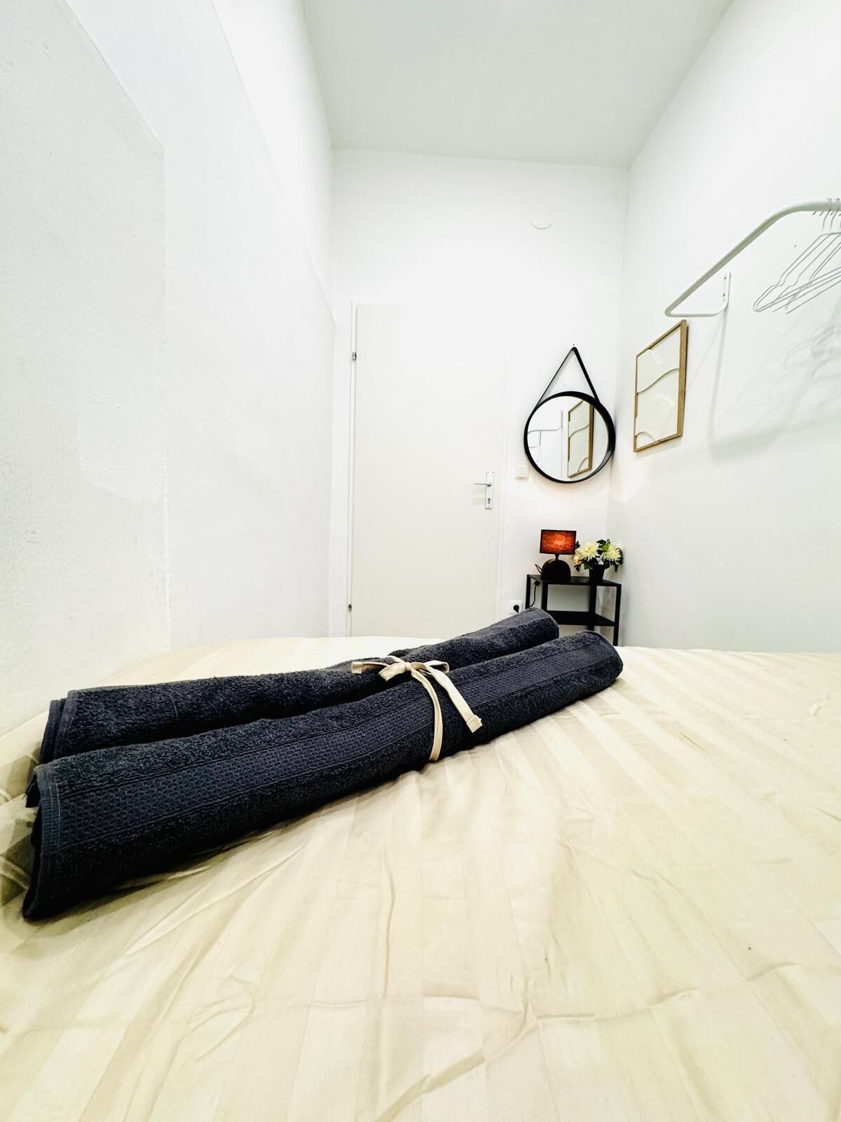 A neatly made bed with a rolled-up towel in a simple, clean room with white walls and minimal decor.