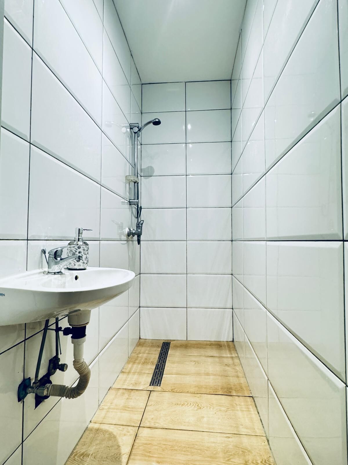 A small, tiled bathroom with a sink and shower.