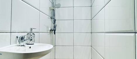 A small, tiled bathroom with a sink and shower.