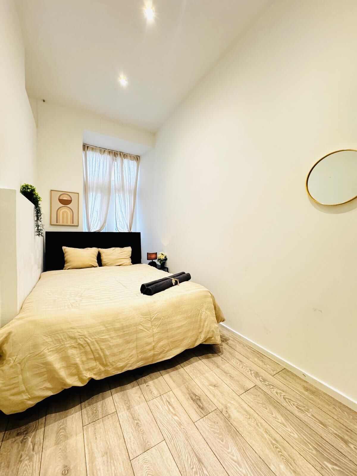Quarto com cama, mesa de cabeceira, espelho e janela com cortinas.