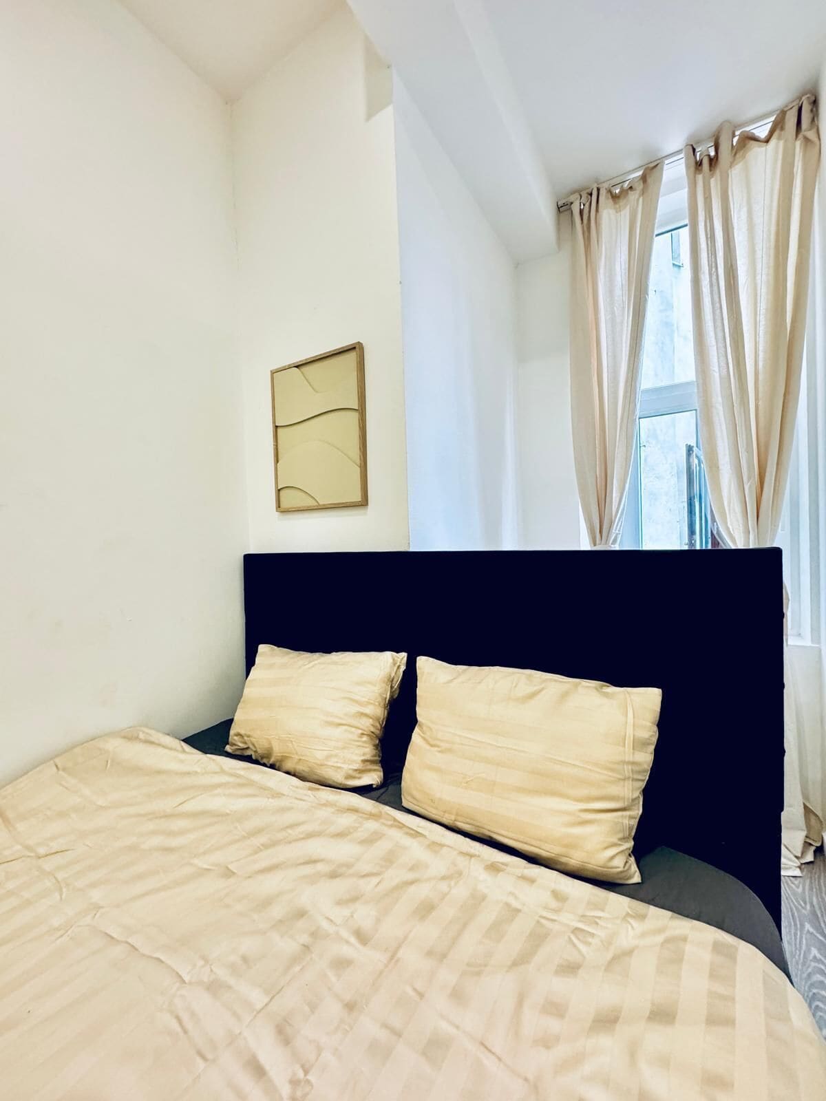 A bedroom with a bed, two pillows, a headboard, a wall-mounted mirror, and a window with curtains.