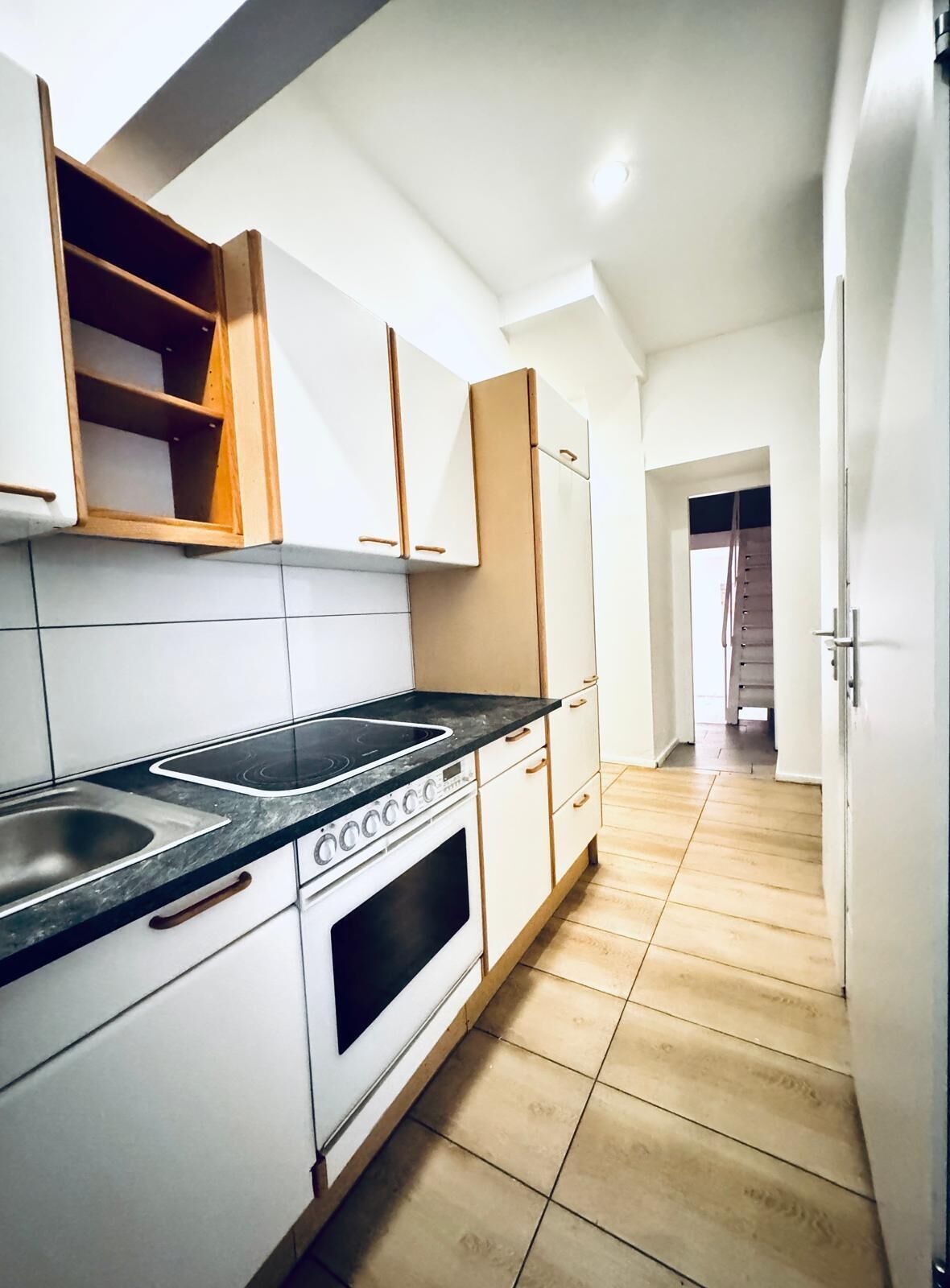 Una cocina moderna con armarios blancos, encimera negra y suelo de madera.