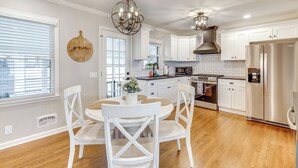 A modern kitchen with white cabinetry, a stainless steel refrigerator, and a dining area with white chairs and a round table.