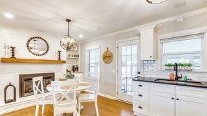 A kitchen with white cabinetry, a wooden dining table with white chairs, a chandelier, and a fireplace.