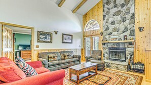 A cozy living room with a fireplace, wooden walls, and a large rug. - 2 Mi to Dtwn: Cloudcroft Home w/ Furnished Deck (Mayhill)