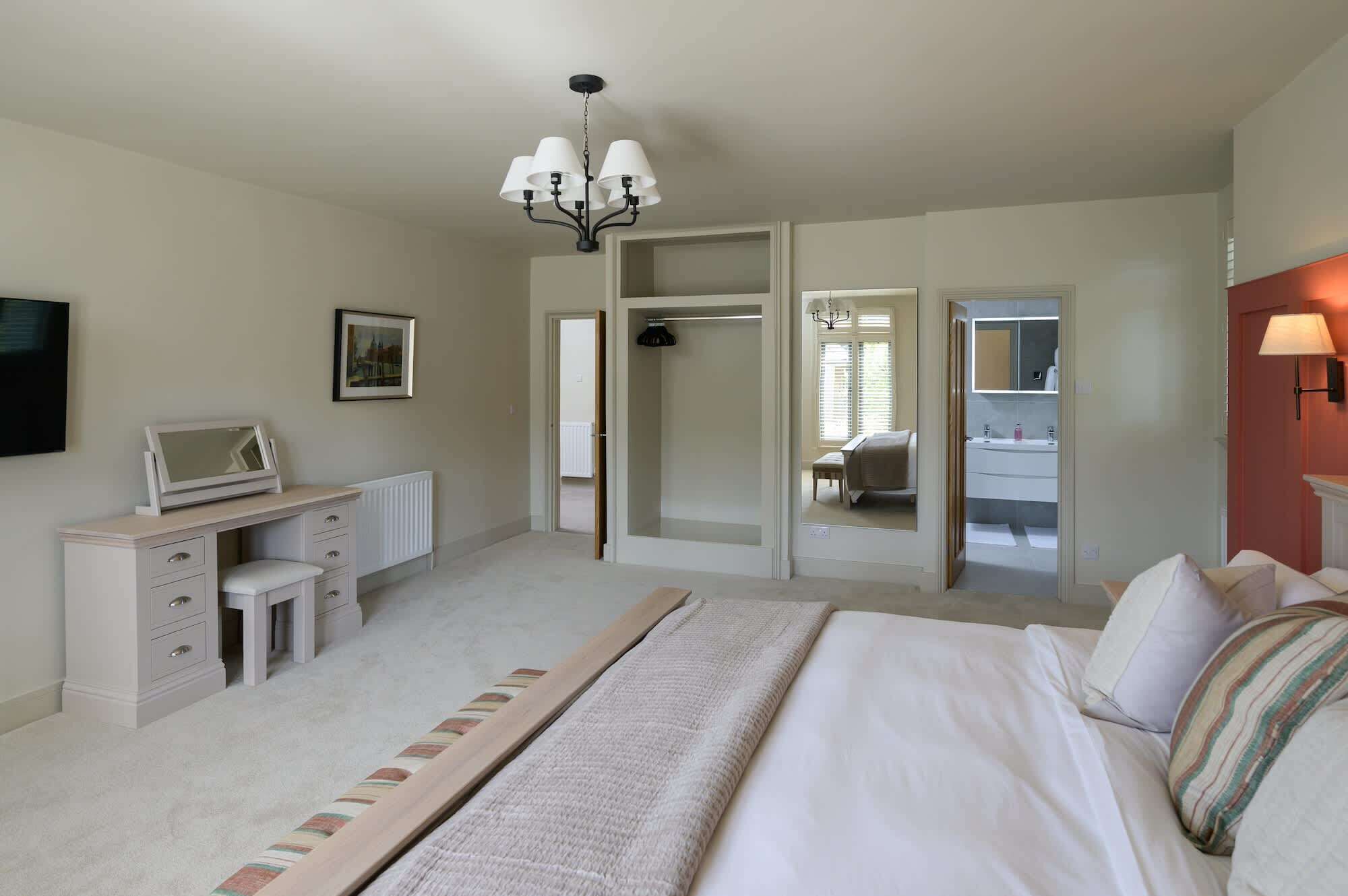 A bedroom with a bed, a desk with a computer, a chair, a wardrobe, and a bathroom visible through a glass door.