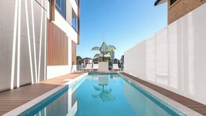A modern pool area with a clear blue pool, wooden deck, and white walls. - Prime Loc! 1BR Apt with Parking Heart of Surfers (Surfers Paradise)
