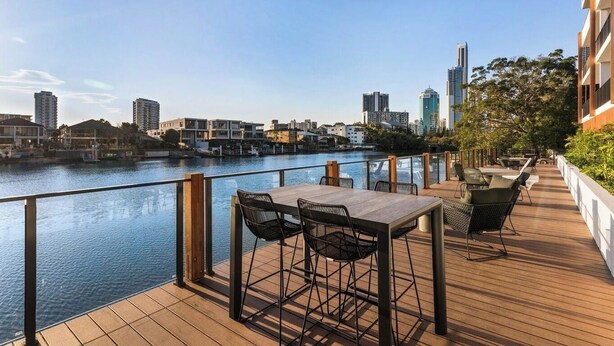 A waterfront deck with a table and chairs, overlooking a river with buildings in the background. - Prime Loc! 1BR Apt with Parking Heart of Surfers (Surfers Paradise)