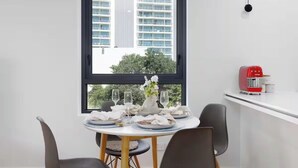 A dining area with a table set for four, a vase with flowers, and a red appliance on a white shelf. - Prime Loc! 1BR Apt with Parking Heart of Surfers (Surfers Paradise)