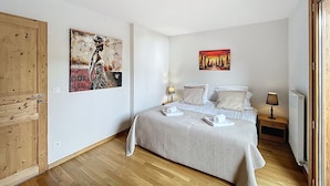 Un dormitorio con cama, dos mesitas de noche, una puerta de madera y dos cuadros colgados en la pared.