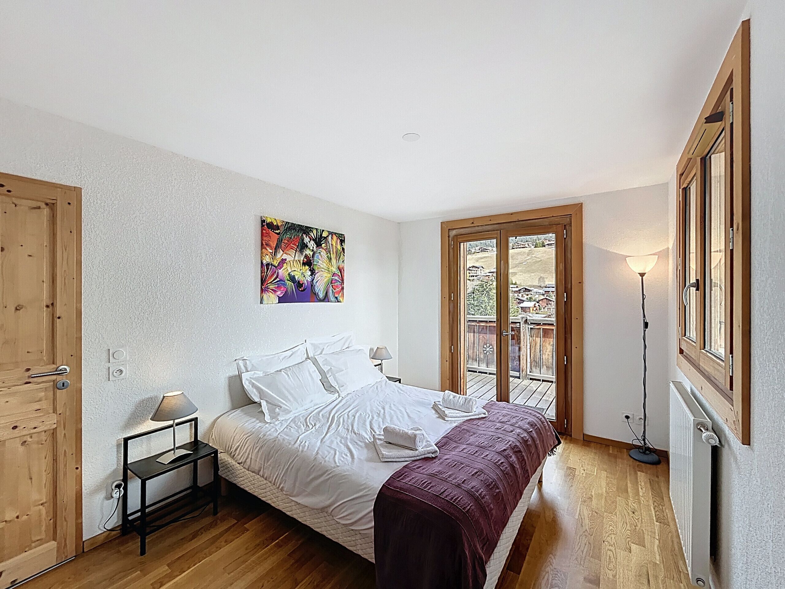 A bedroom with a bed, a nightstand, a lamp, a painting, and a view through a door.