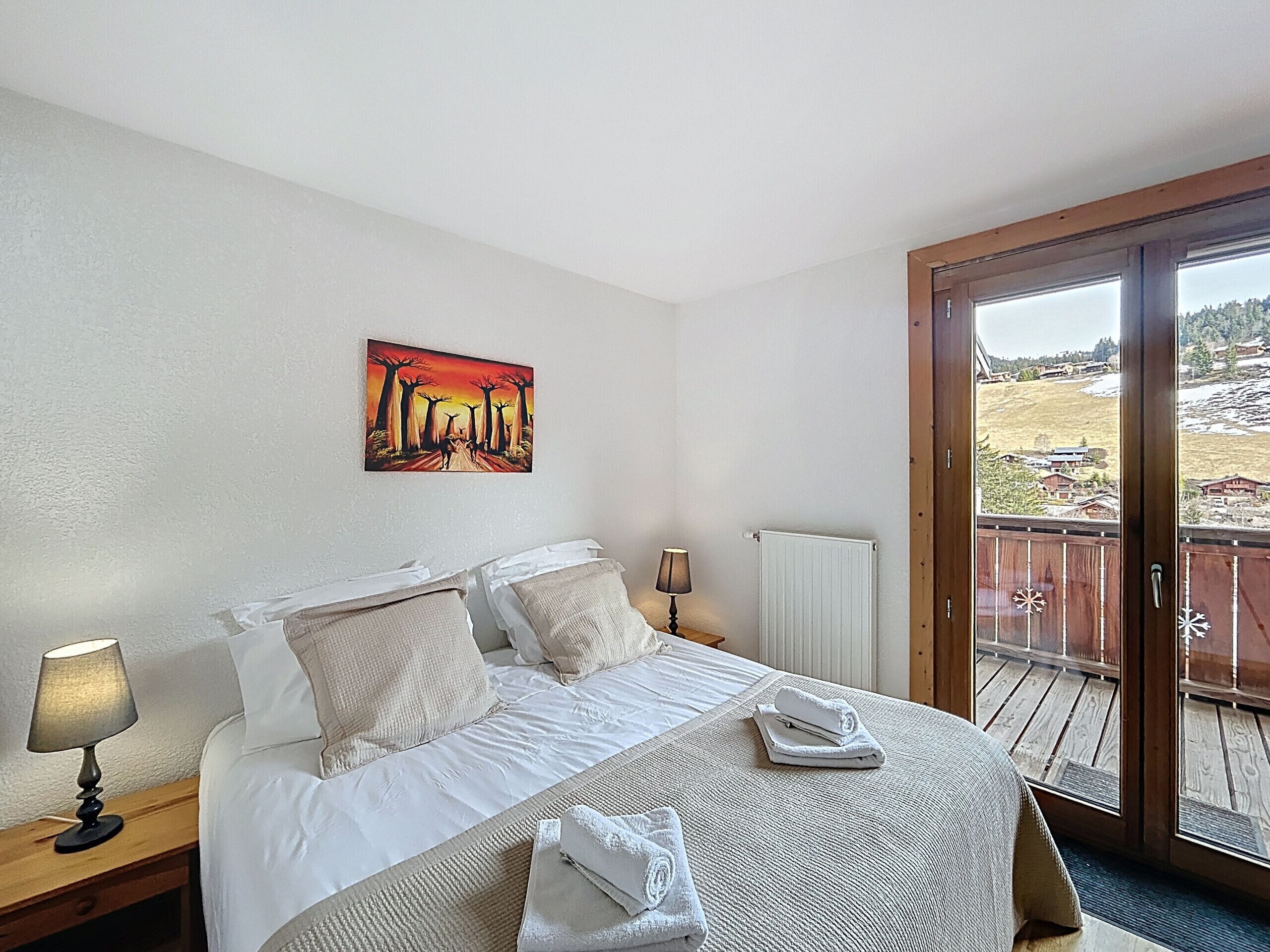 A hotel room with a bed, a painting, a lamp, and a view of a snowy landscape through a sliding door.