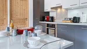 Una cocina moderna con armarios grises, una puerta de madera, una mesa de comedor con platos y tazones blancos, y una cafetera.