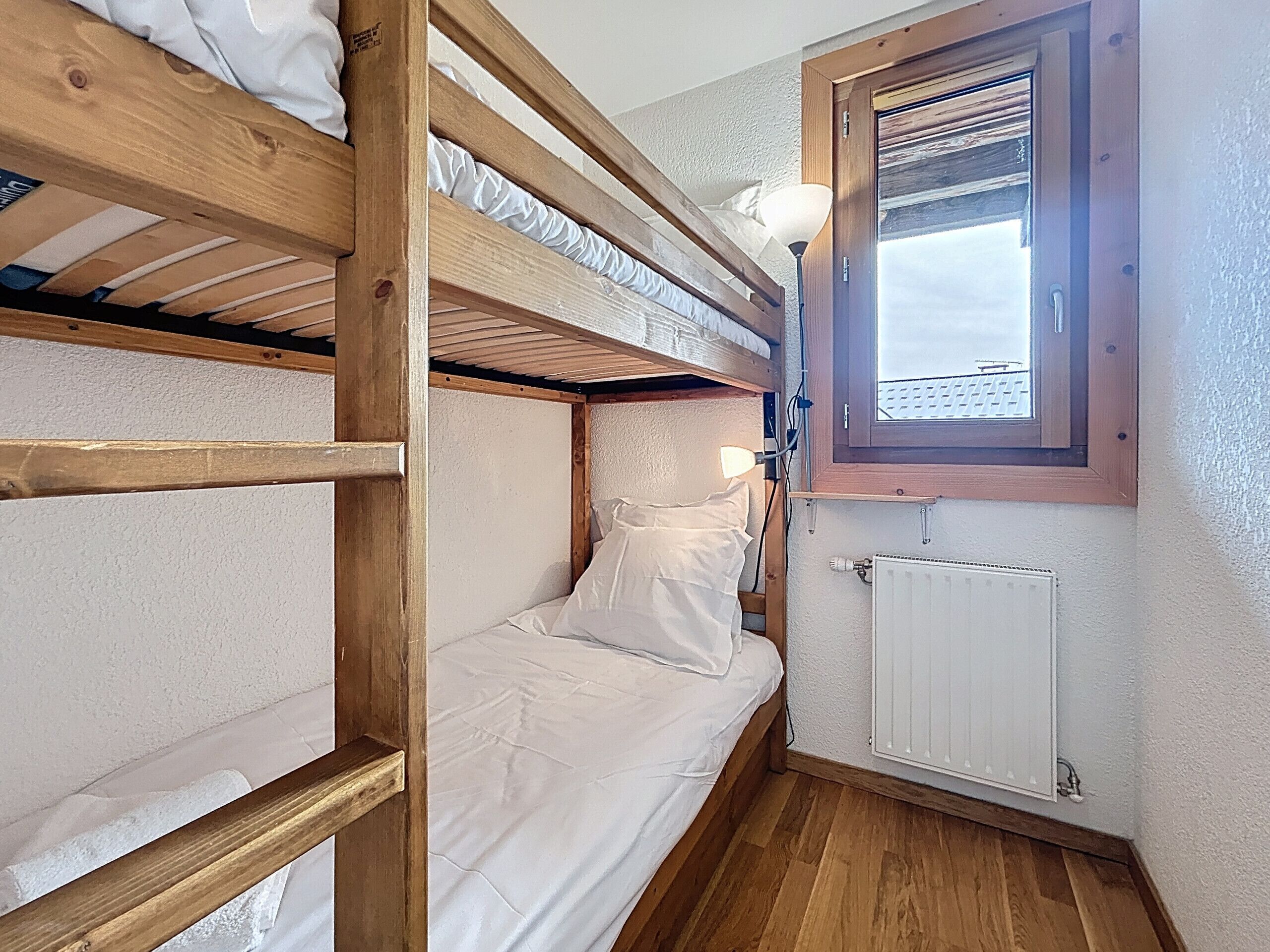 Ein Schlafraum mit Etagenbett, Fenster, Heizkörper und Lampe.