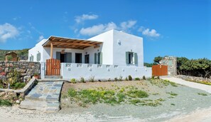 A modern white building with a stone wall, wooden gate, and a stone pathway leading to the entrance.
