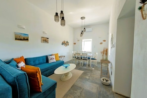 A modern living room with a blue sofa, a white coffee table, and a dining area with a white table and chairs.