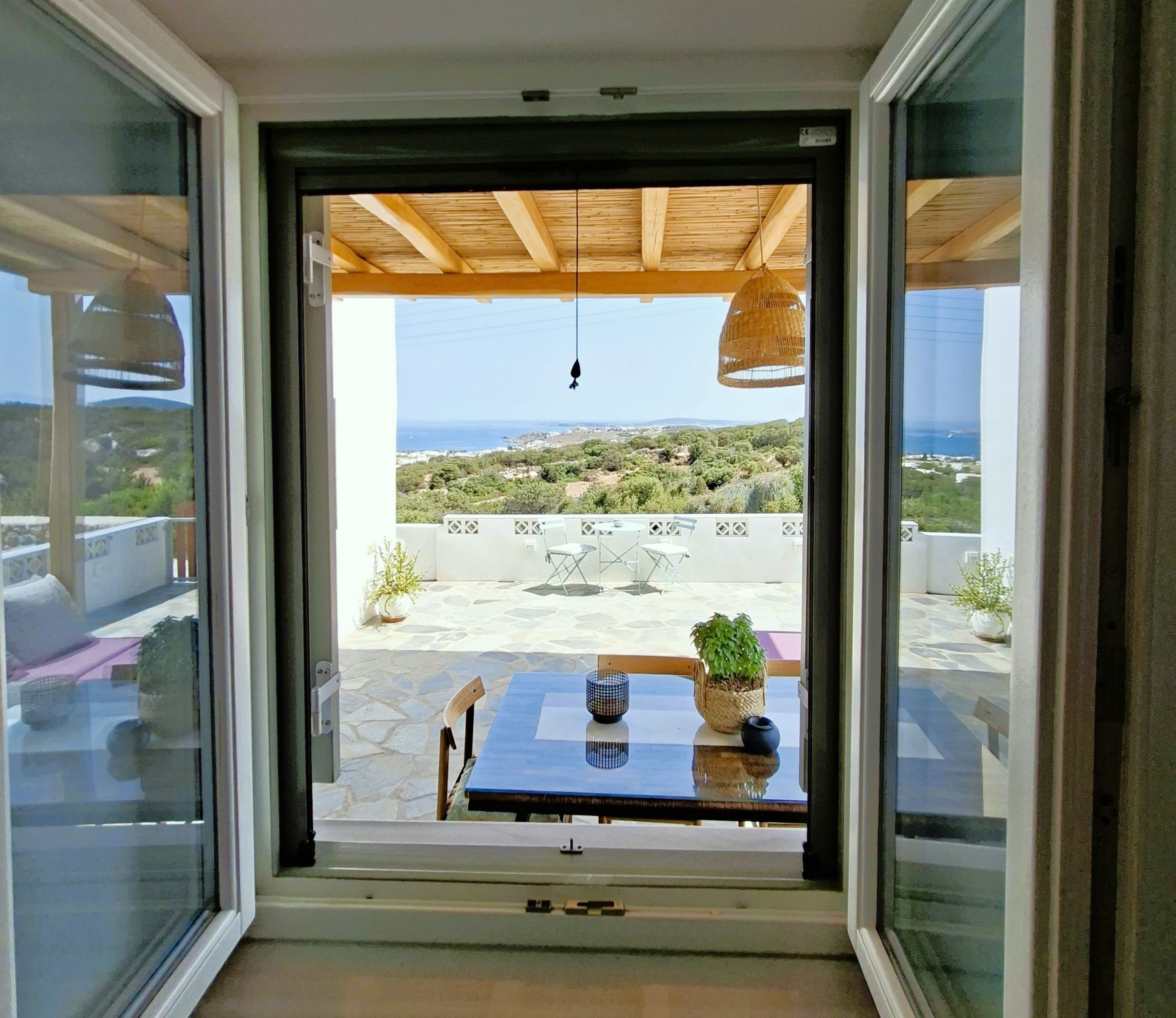 A view from a room with a glass door leading to an outdoor patio with a table, chairs, and potted plants.
