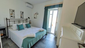 Ein Schlafzimmer mit Bett, Nachttisch, Klimaanlage, Fernseher und Blick durch eine Tür nach draußen.