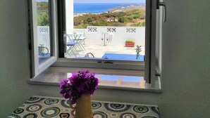 Ein Fenster mit Blick auf eine Terrasse, ein Tisch mit Blumenvase und einer gemusterten Tischdecke.