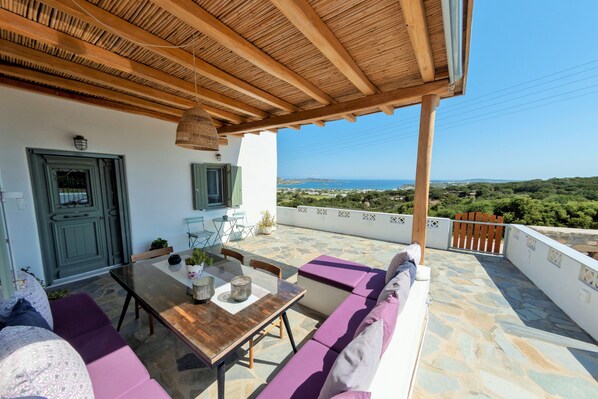 A covered outdoor seating area with a table and chairs, a wooden ceiling, and a view of the landscape.