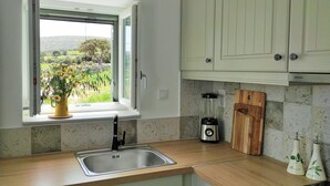 Eine Küche mit Fenster, Spüle, Mixer, Schneidebrett aus Holz und dekorativen Vasen.