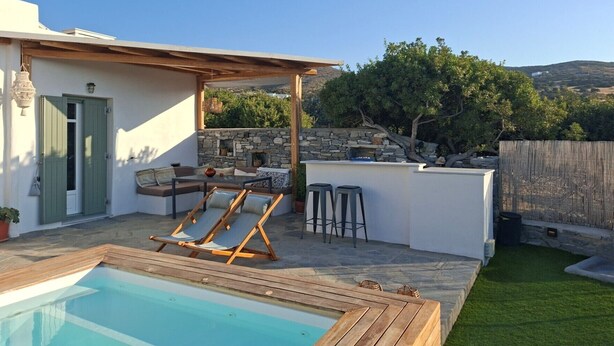 Ein Poolbereich mit Holzterrasse, Steinmauer und einer Sitzgelegenheit mit Tisch und Stühlen.