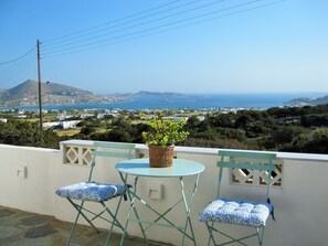 A balcony with a table and two chairs, overlooking a coastal town with a mountain in the background.