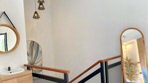 A modern interior with a staircase, a wooden-framed railing, a round mirror, and pendant lighting. - DIRUMA SADJA HOME VILLA (Ngemplak)