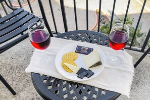 Ett bord med en tallrik med ost, kex och choklad, tillsammans med två glas rött vin, placerat på en balkong med utsikt över palmer.