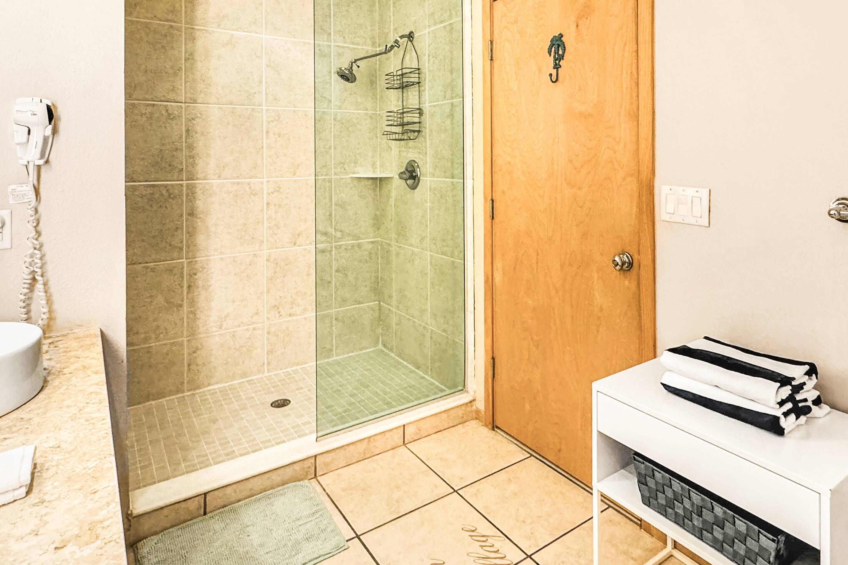 Un baño con ducha de vidrio, puerta de madera, lavabo blanco y un armario con toallas.