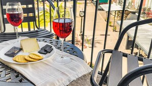Una mesa con un plato de queso, galletas y dos copas de vino tinto, en un balcón con vistas a edificios y vegetación.