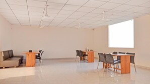 A spacious room with two wooden tables and chairs, a sofa, and a large window providing natural light. - Hotel Fun Regency (Mandal)