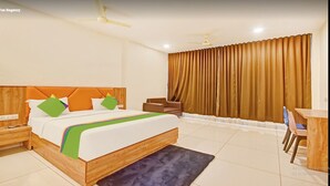 A hotel room with a large bed, a desk, a chair, a nightstand, and a window with curtains. - Hotel Fun Regency (Mandal)