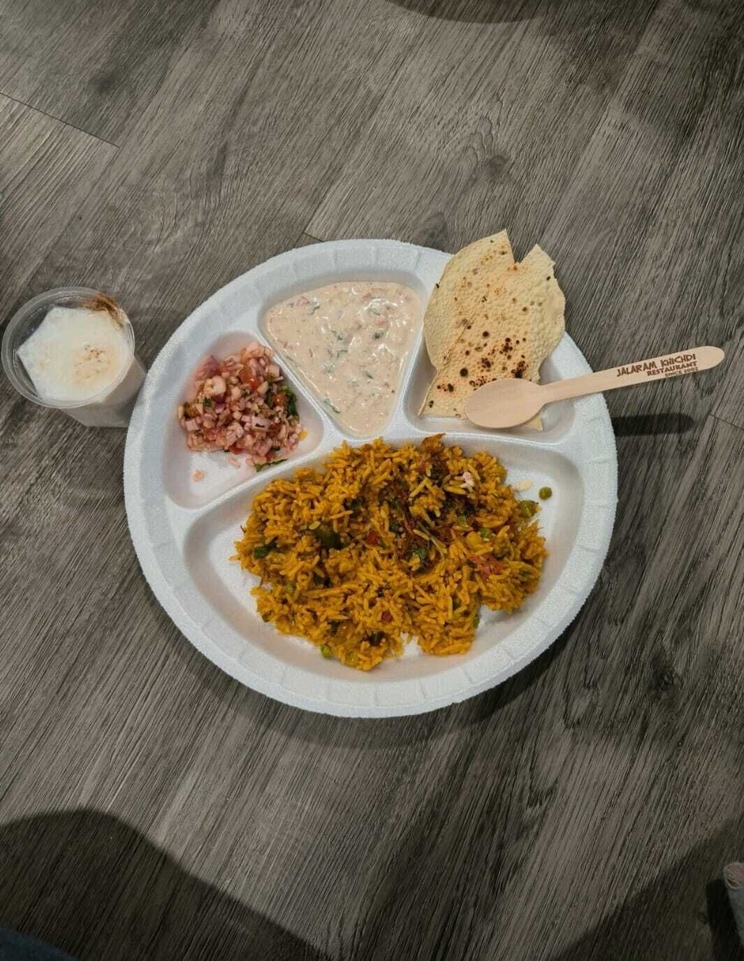 Un plato de papel con una comida que incluye arroz, salsa cremosa, un recipiente pequeño de vegetales picados y un pedazo de pan plano.