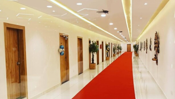 A hotel corridor with a red carpet, wooden doors, and wall-mounted decorations. - Hotel Fun Regency (Mandal)