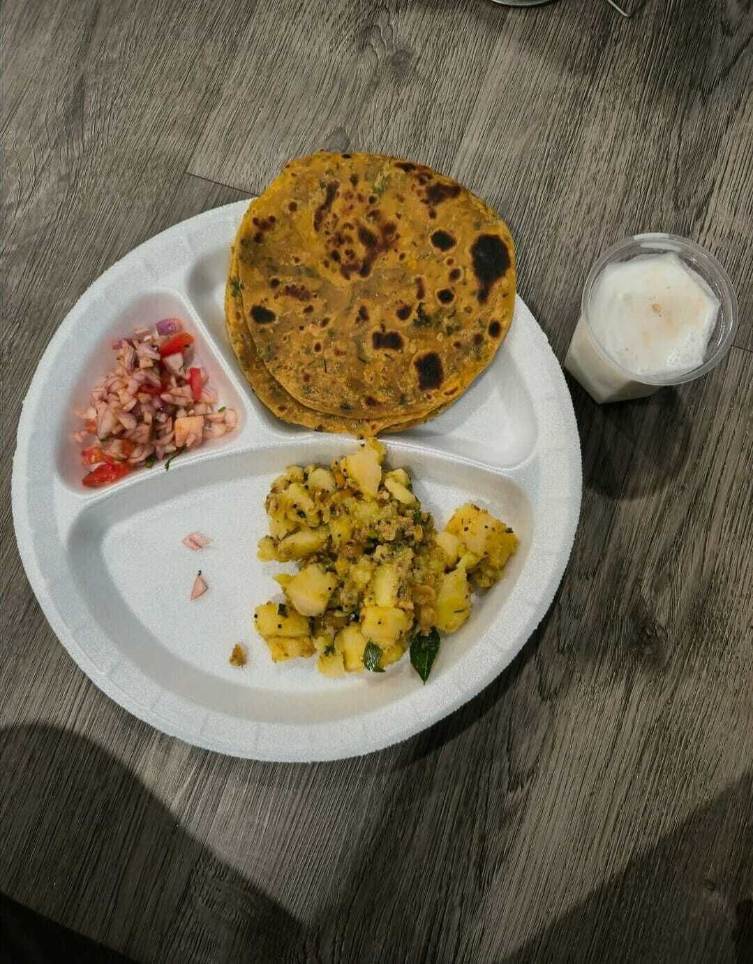 A meal consisting of a flatbread, a side of potato salad, and a small container of yogurt on a white plate.