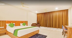 Ein Hotelzimmer mit einem großen Bett, einem Schreibtisch, einem Stuhl, einem Nachttisch und einem Fenster mit Vorhängen.