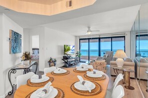 A modern living room with a dining area, large windows, and a view of the sea.